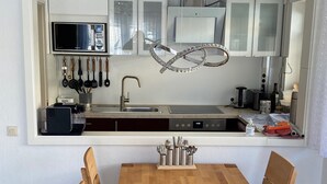 Une cuisine moderne avec des meubles blancs, une table à manger en bois et un lustre suspendu.