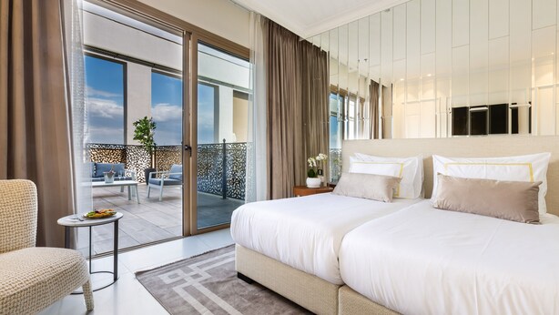 Una habitación de hotel moderna con una cama grande, una mesita, una silla y un balcón con mobiliario exterior.