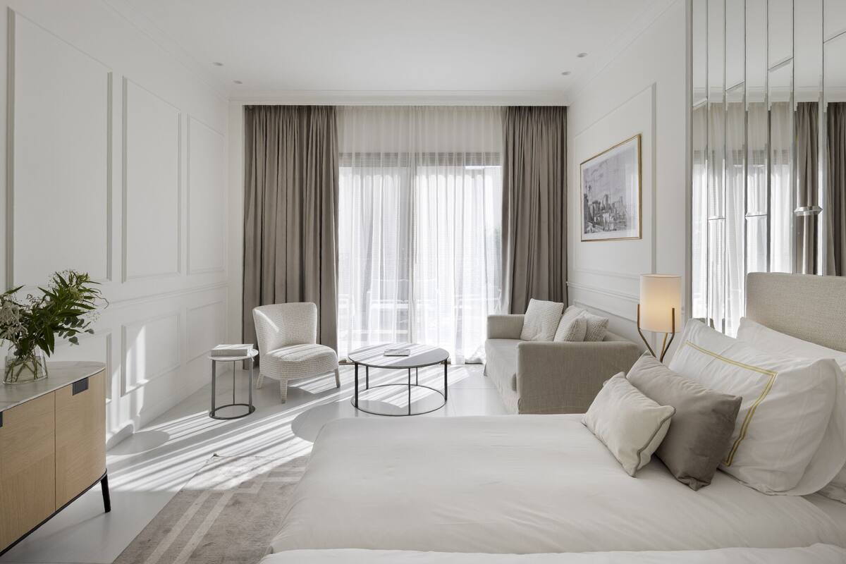 Moderni hotellihuone, jossa on suuri sänky, kaksi nojatuolia, pieni pyöreä pöytä ja sohva.