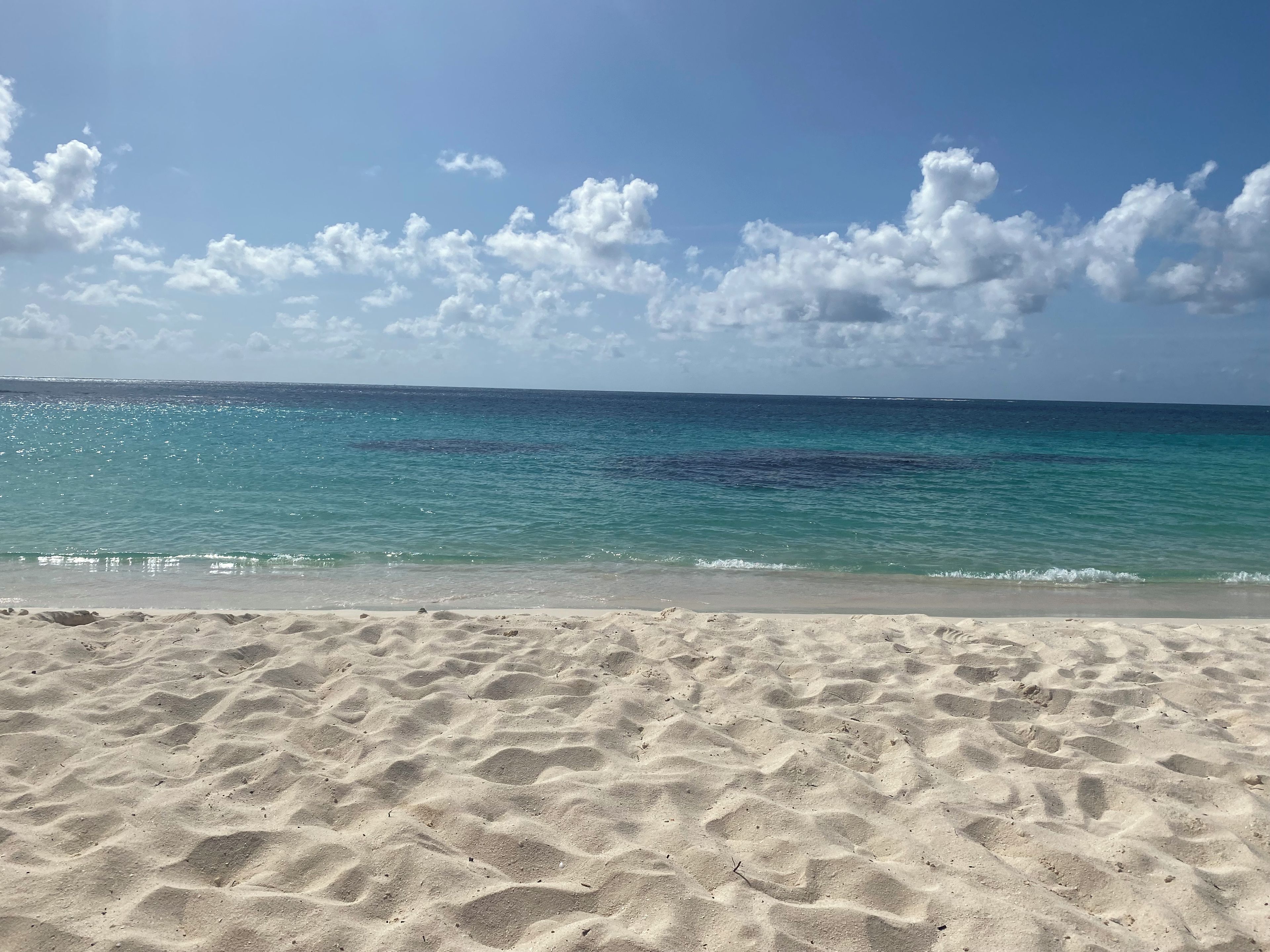 A sandy beach with clear blue water and scattered clouds.