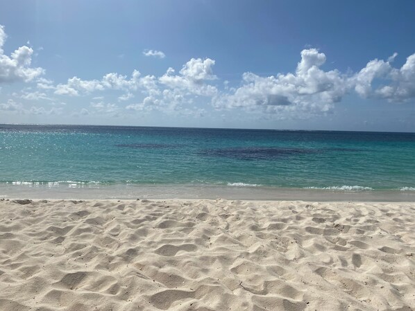 A sandy beach with clear blue water and scattered clouds.