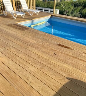 A wooden deck with a swimming pool and white lounge chairs.