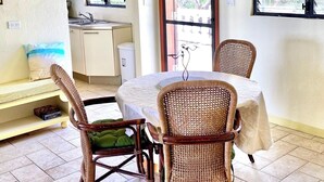 Uma área de refeições com cadeiras de vime, uma mesa redonda e vista para a cozinha e área externa.