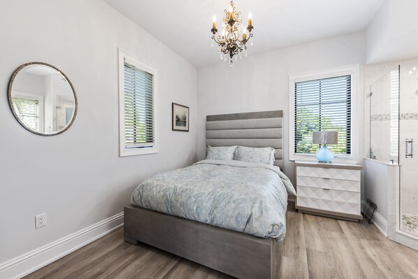 A bedroom with a bed, bedside table, dresser, and a chandelier.