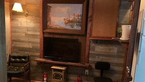 Un salon chaleureux avec une cheminée, des murs en bois, un téléviseur et une petite table.