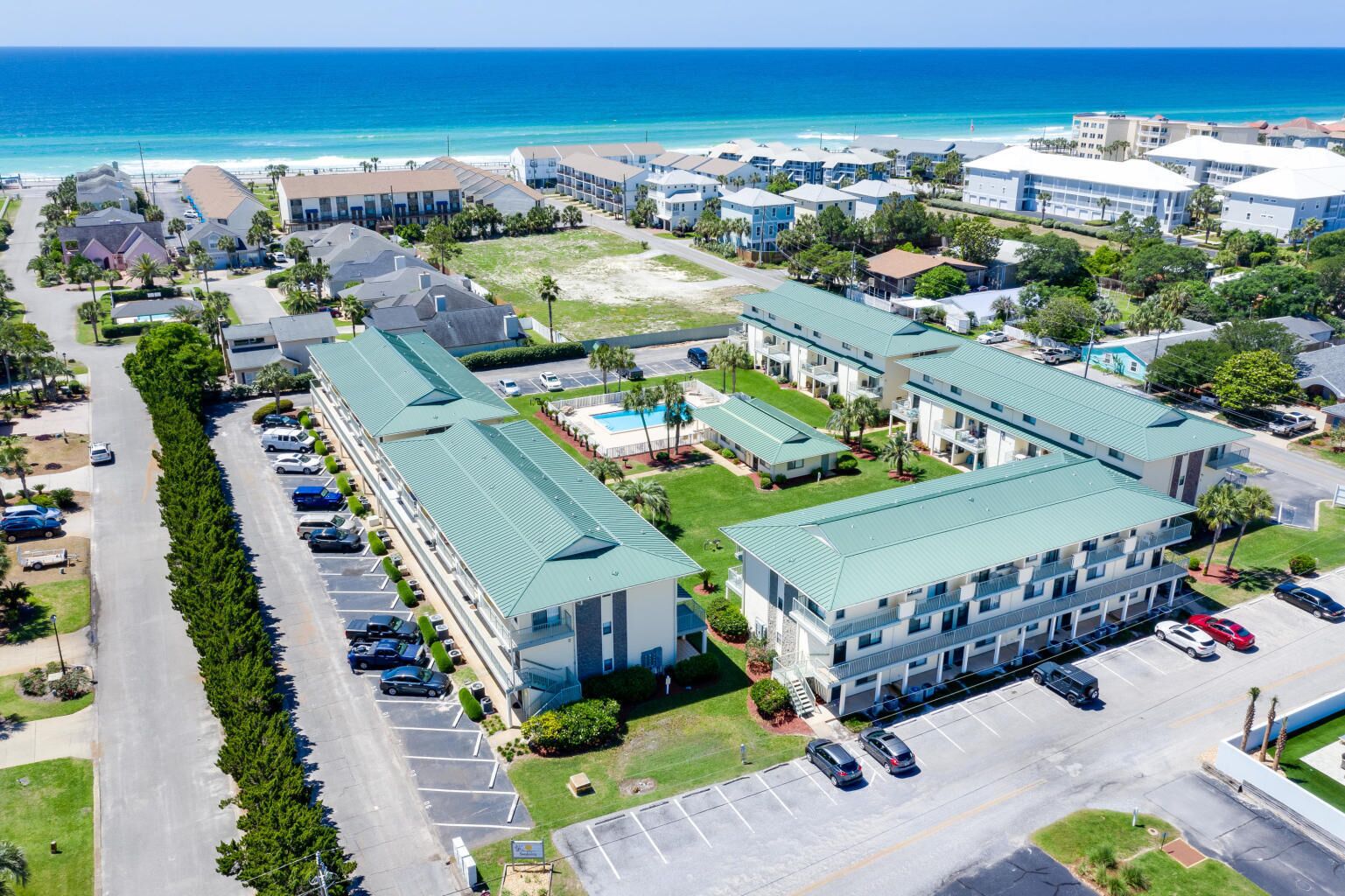An aerial view of a coastal hotel complex with multiple buildings, parking areas, and a view of the ocean.
