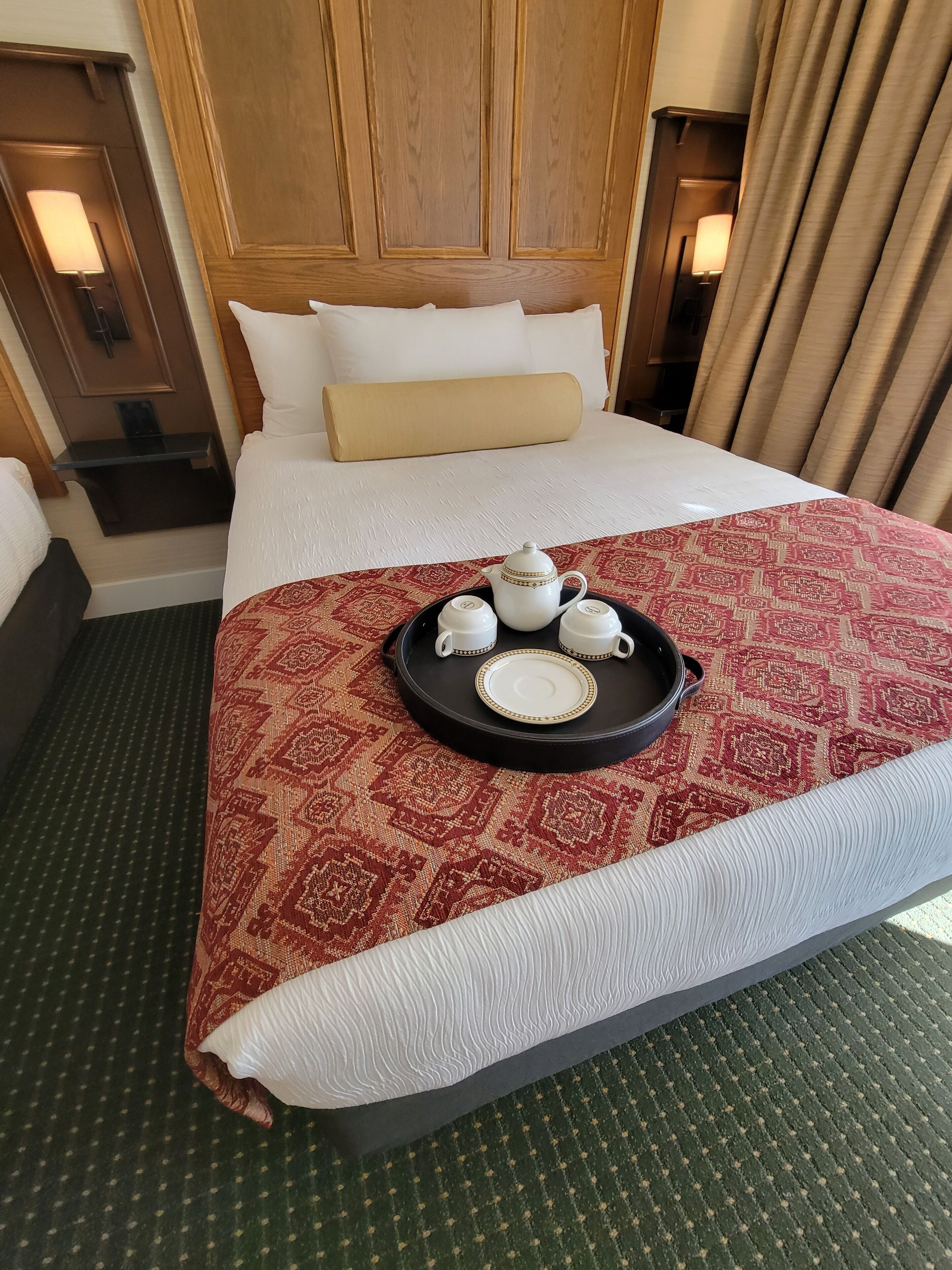 A hotel room with a large bed, a tray with tea set, and a patterned bedspread.
