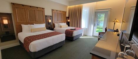 A hotel room with two beds, a desk, a mirror, and a sliding glass door to the outside.