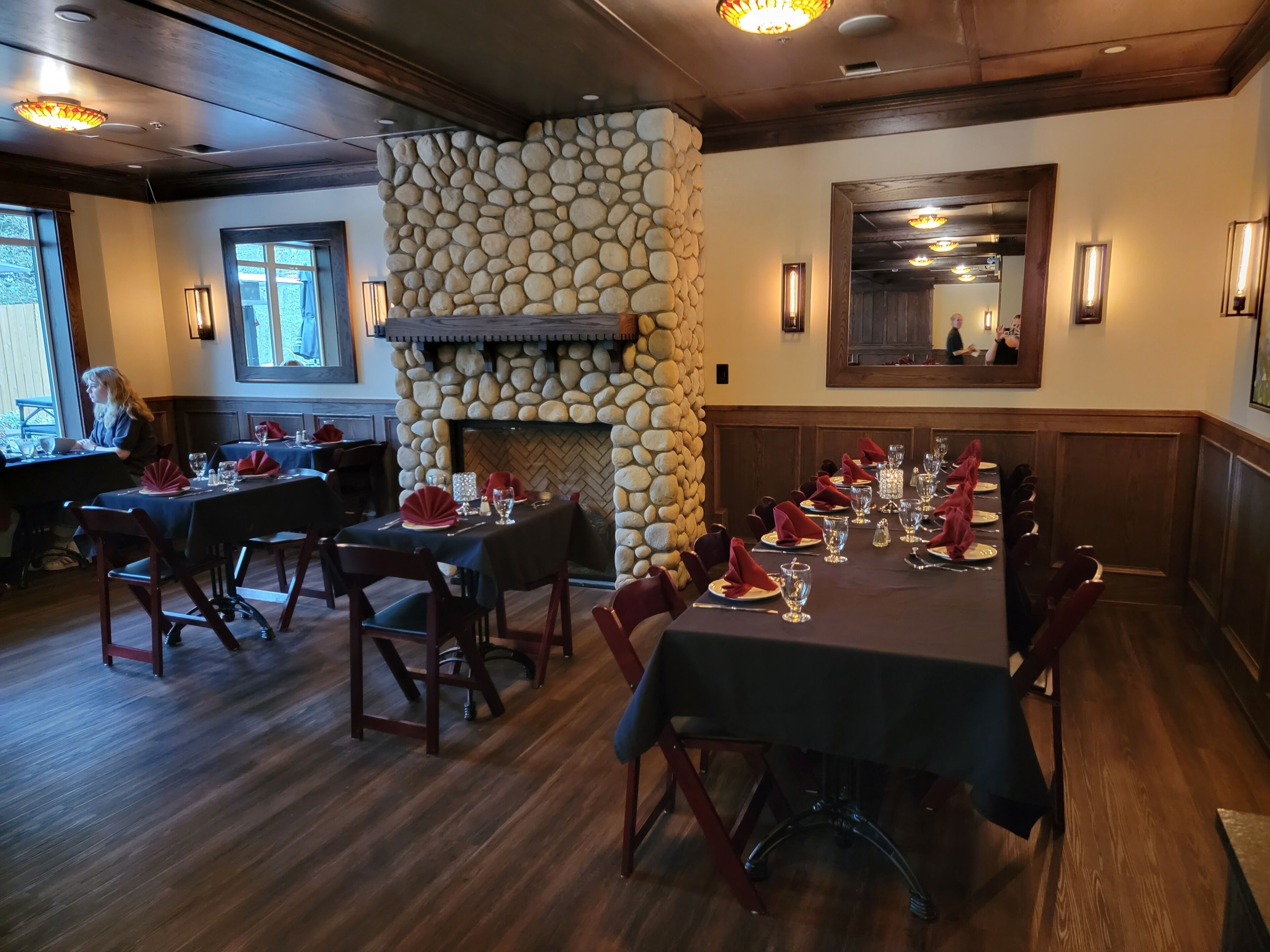 A restaurant with a stone fireplace, wooden ceiling, and tables set for dining.