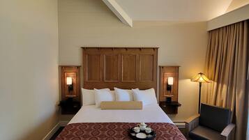 A hotel room with a large bed, two bedside tables with lamps, a chair, and a tray with teapots and cups.