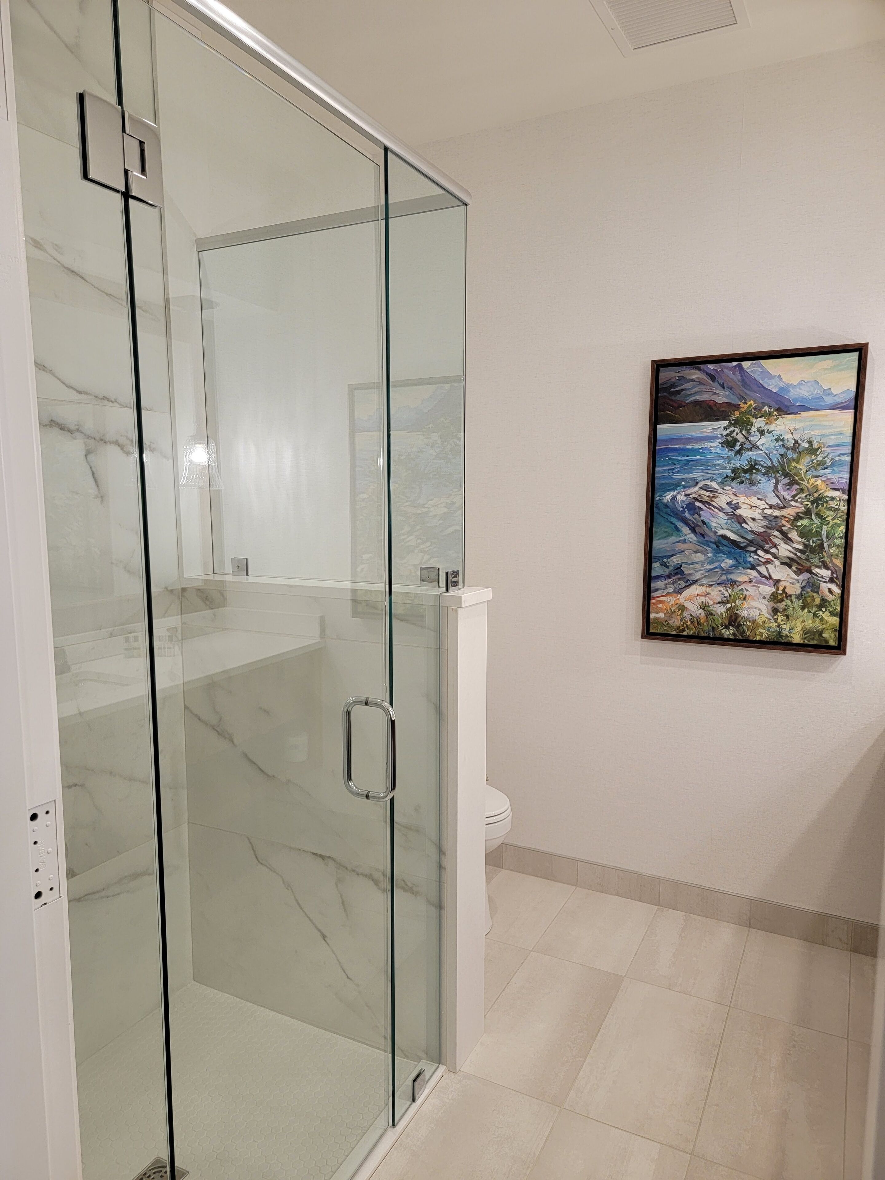 Een moderne badkamer met een douchecabine van glas, een toilet en een landschapsschilderij aan de muur.