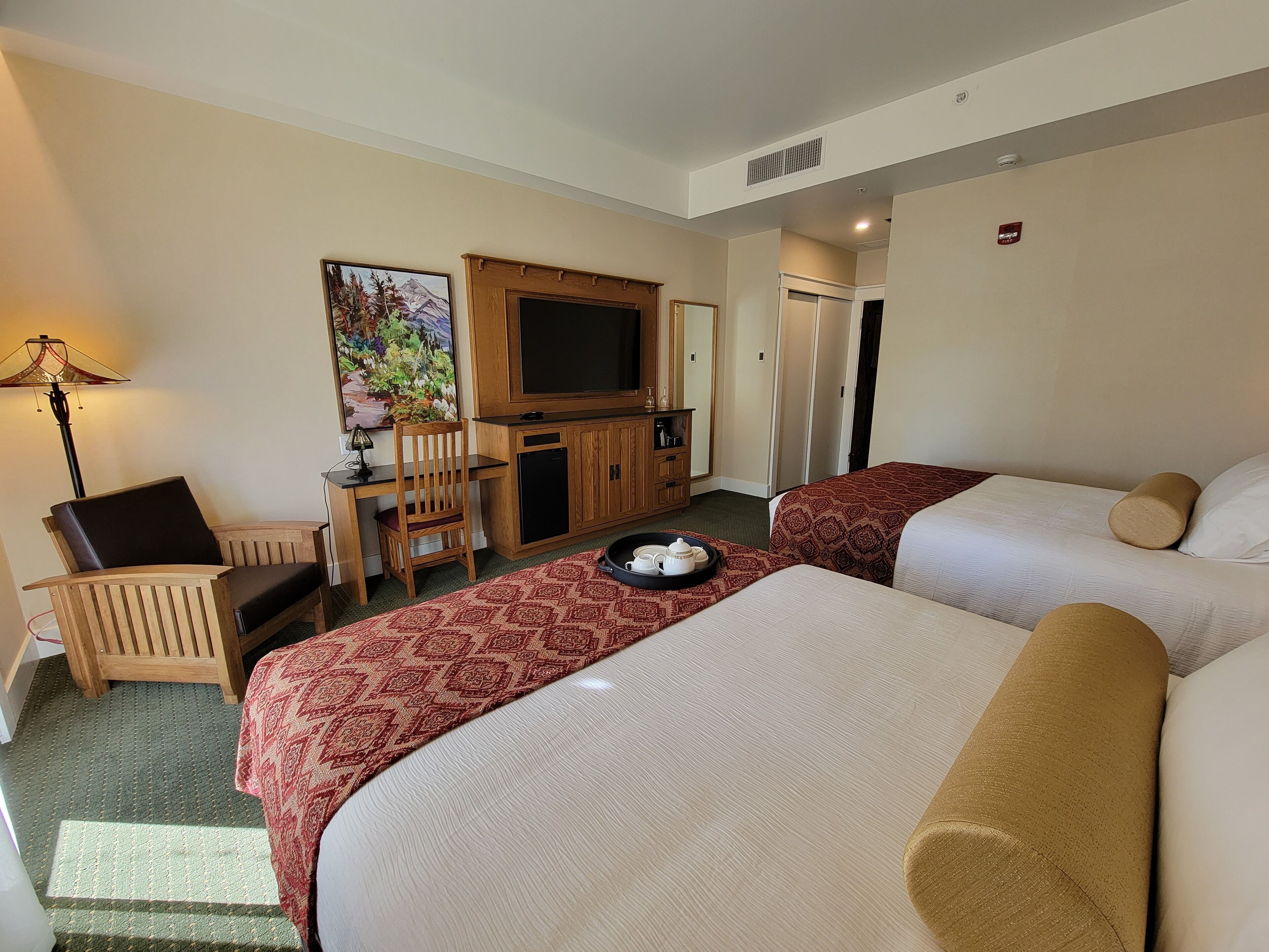 A hotel room with two beds, a desk with a chair, a television, and a painting on the wall.