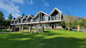 A multi-story building with a stone facade, balconies, and a well-maintained lawn. - Kilmorey Lodge (Waterton Park)