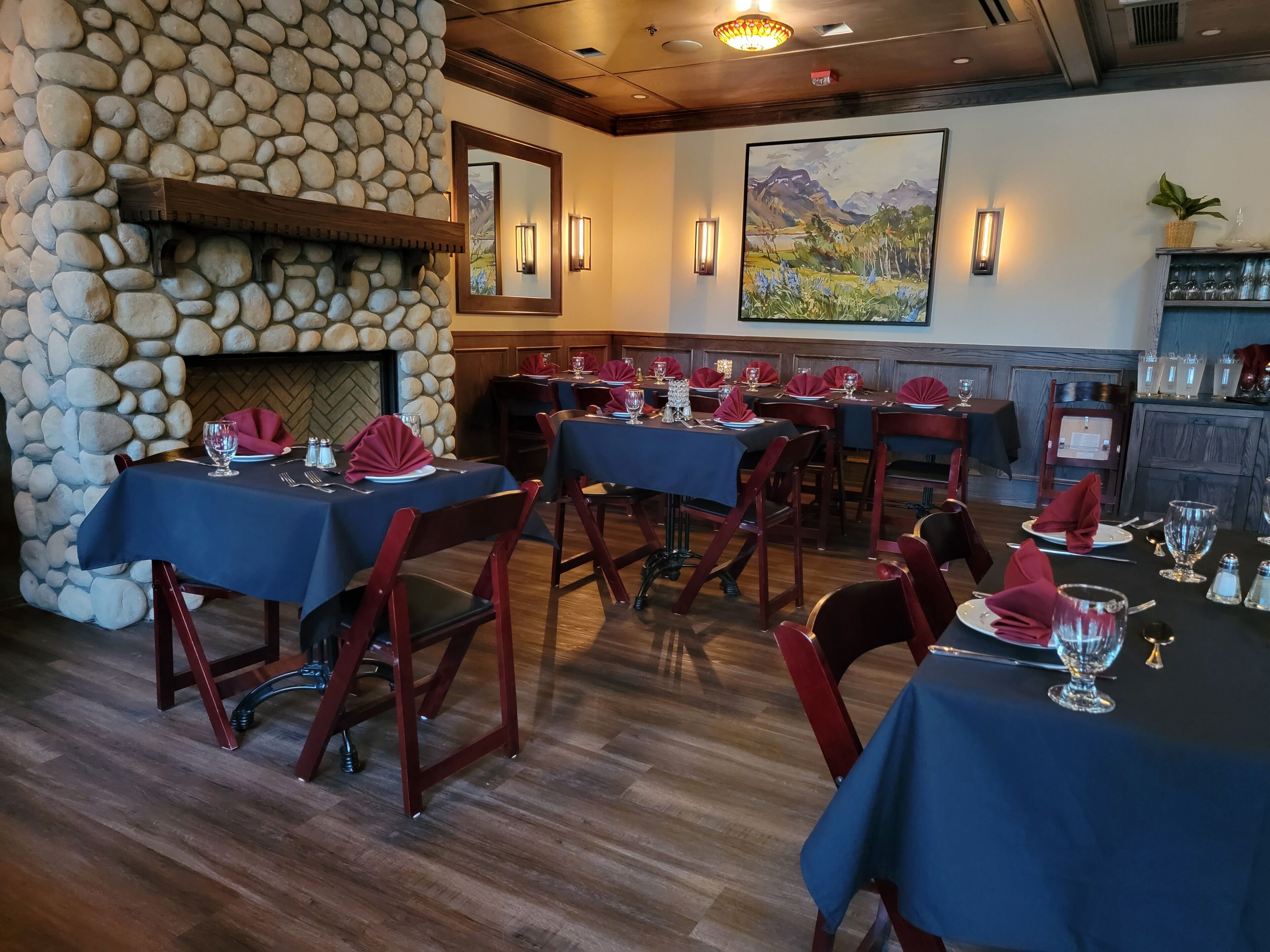 A restaurant with stone walls, wooden tables, and red chairs.