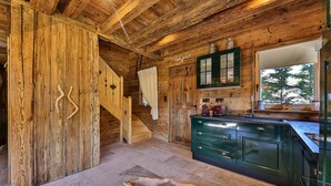 A rustic cabin interior with wooden walls, a stone floor, a green kitchen with cabinets, and a fur rug. - Chalet Hohneck 4**** old wood and stone, SPA, sauna, charging station (Stosswihr)