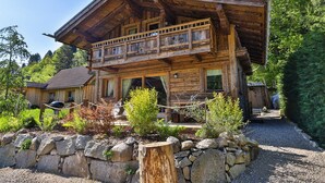 A wooden cabin with a balcony, surrounded by a stone wall and greenery. - Chalet Hohneck 4**** old wood and stone, SPA, sauna, charging station (Stosswihr)