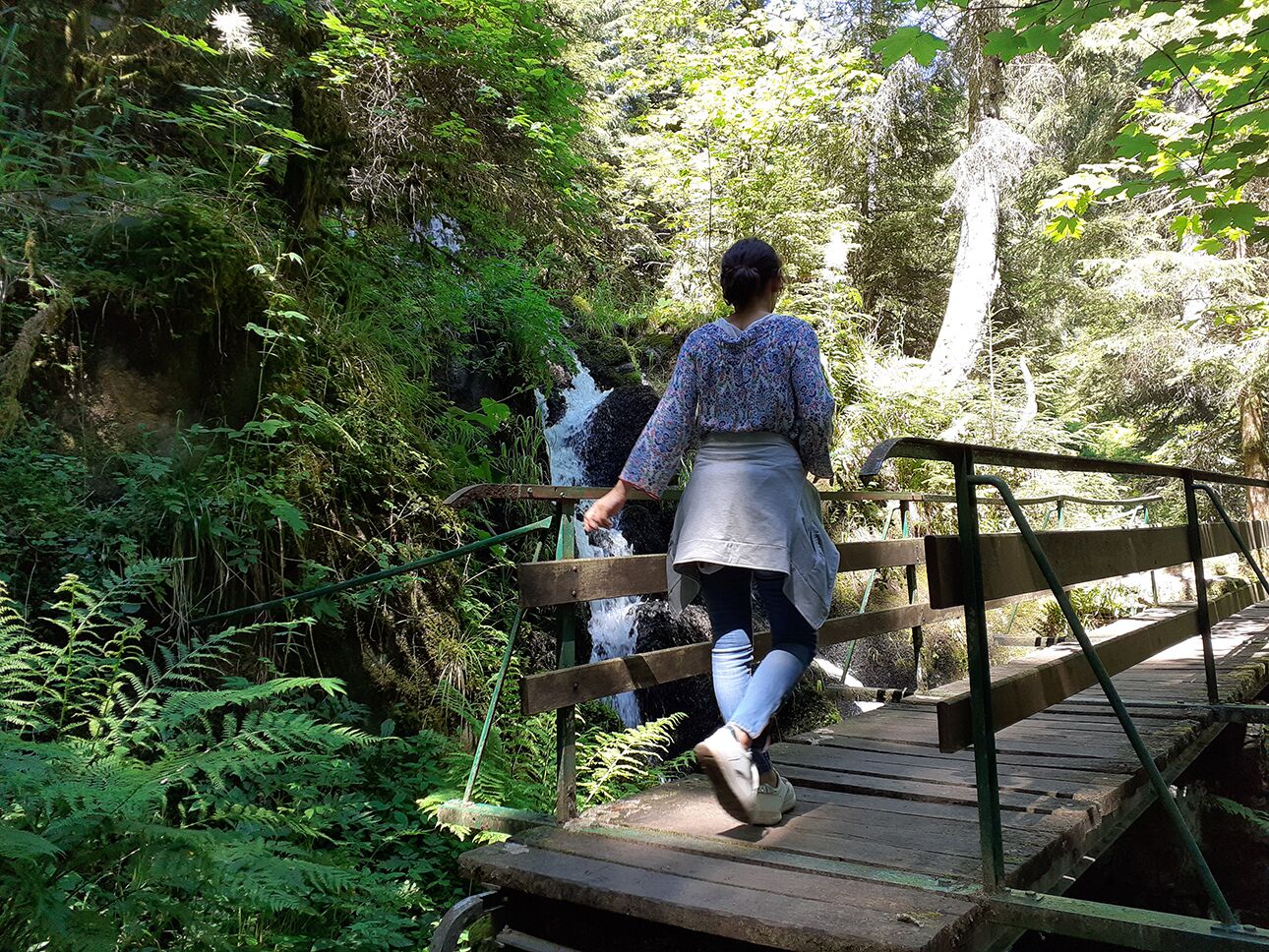 A person walking on a wooden bridge in a forested area.