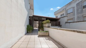 A narrow courtyard with tiled flooring, a covered walkway, and potted plants.