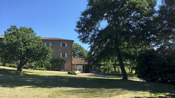 Un edificio de piedra con techo de tejas, rodeado de césped cuidado y árboles.