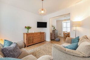A living room with a wooden cabinet, a flat-screen TV, and a sofa with cushions. - Postman's Cottage (Bridlington)