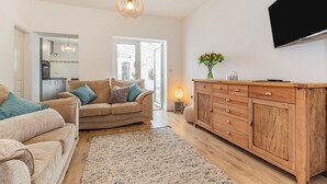 A living room with a sofa, a wooden cabinet, and a television. - Postman's Cottage (Bridlington)