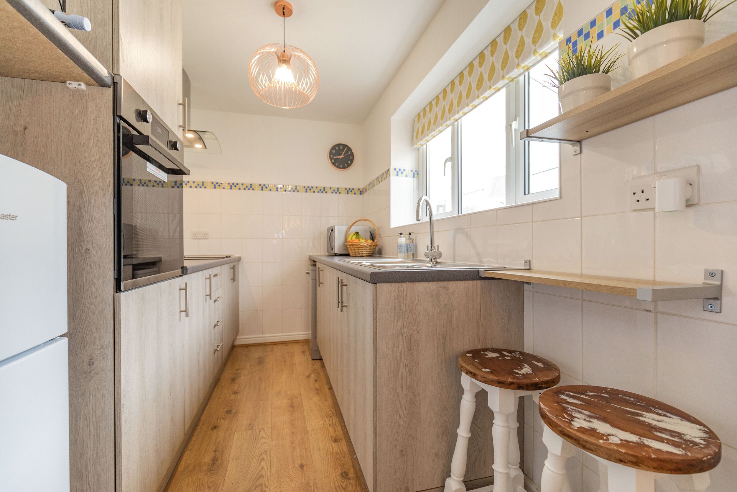 A kitchen with wooden cabinets, a built-in oven, a sink, and two stools.
