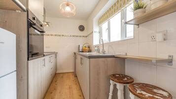 A kitchen with wooden cabinets, a built-in oven, a sink, and two stools.