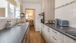 A modern kitchen with a wooden cabinet, a built-in oven, and a countertop with a toaster and kettle. - Postman's Cottage (Bridlington)