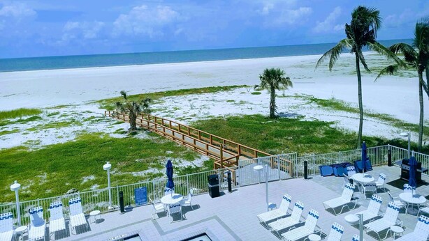 A beachside patio with lounge chairs and umbrellas, a wooden walkway, and a view of the ocean.