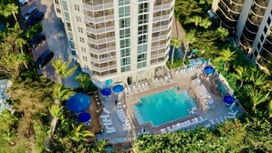 A high-rise hotel with a rooftop pool surrounded by palm trees and lounge chairs.