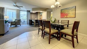 A spacious hotel room with a dining area, a balcony with a view, and a ceiling fan.