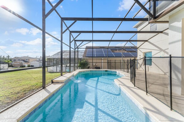 Relax by the pool surrounded by a lush lawn and a building with solar panels.