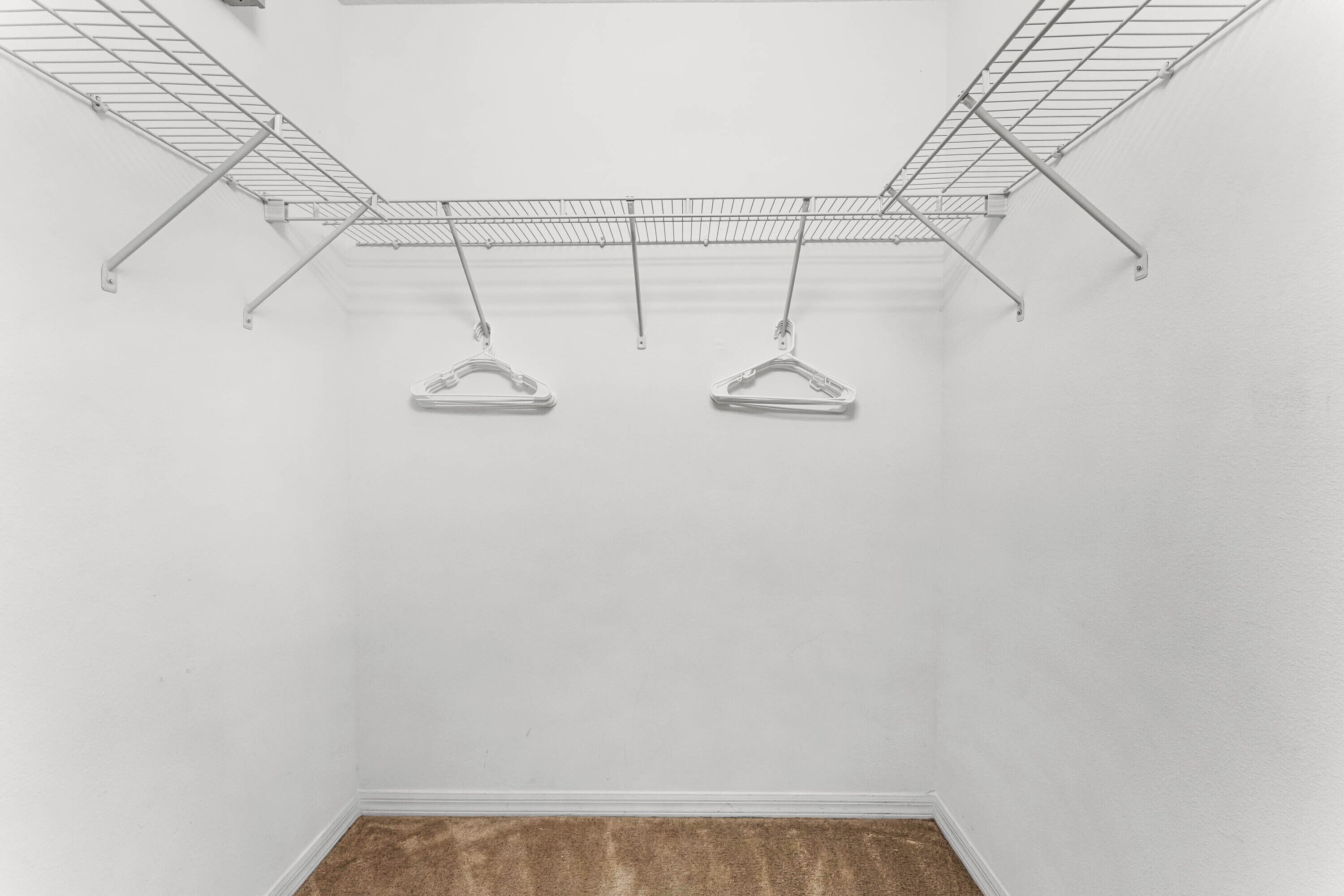 Un placard blanc avec une étagère en fil métallique et deux cintres en plastique vides.