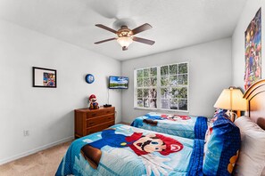 Ein Schlafzimmer mit zwei Betten, einem Deckenventilator, einem Fernseher, einer Kommode und einem Fenster mit Jalousien.