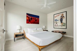 Une chambre avec un lit simple, deux tables de chevet, un ventilateur de plafond et une affiche accrochée au mur.