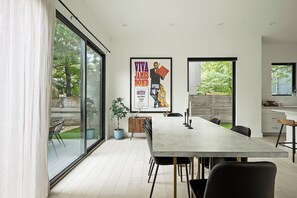 A modern dining area with a long table, chairs, and a large poster on the wall. - East Austin Oasis | Pool | Grill | Modern 4BR Home (Austin)