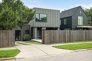 A modern two-story house with a grey exterior, a wooden fence, and a well-maintained lawn. - East Austin Oasis | Pool | Grill | Modern 4BR Home (Austin)