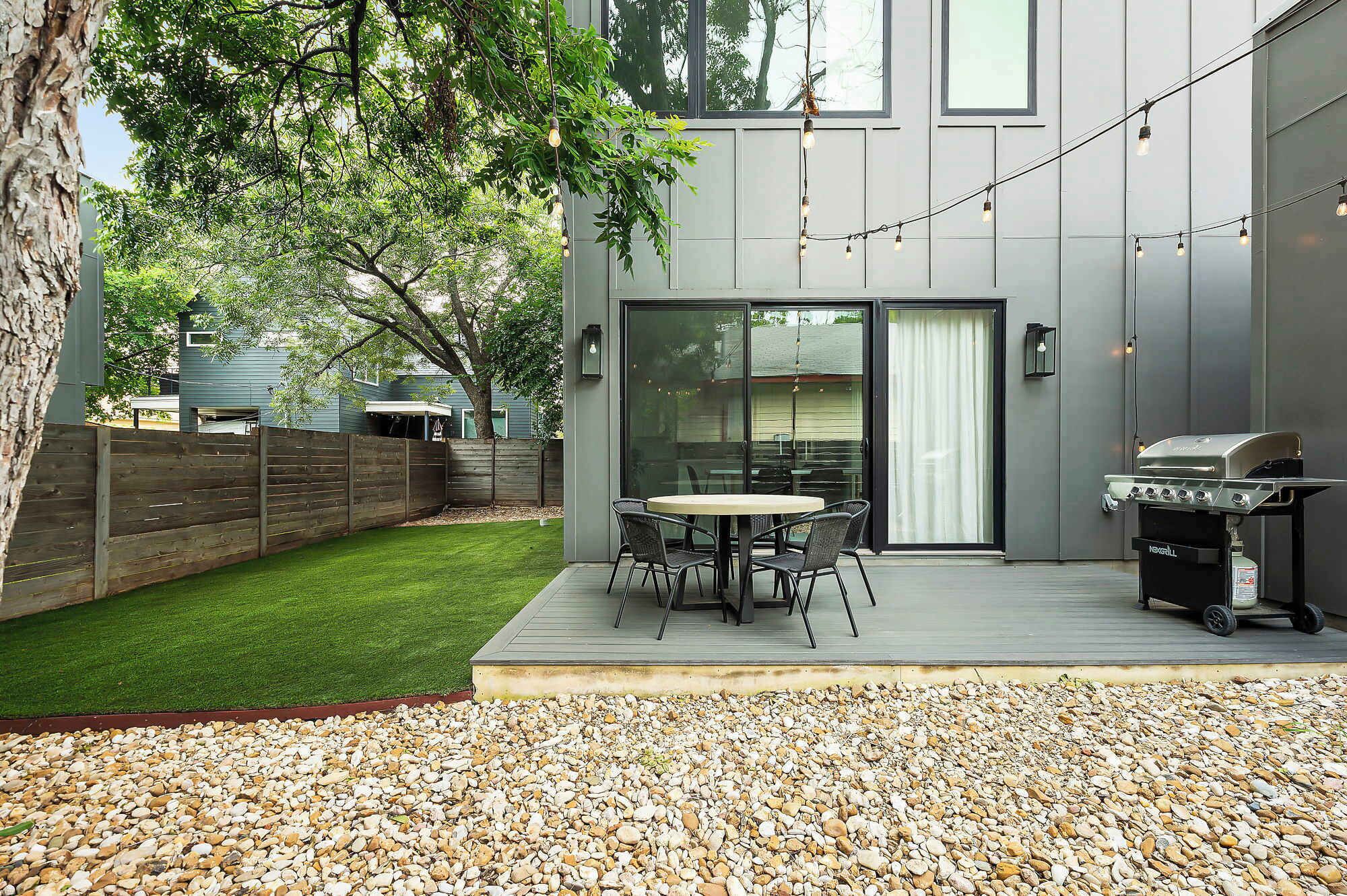 A modern patio with a round table and chairs, a barbecue grill, and a wooden fence.