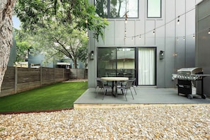 A modern patio with a round table and chairs, a barbecue grill, and a wooden fence. - East Austin Oasis / Pool / Grill / Modern 4BR Home (Austin)