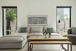 A modern living room with a sofa, a coffee table, and a large abstract painting on the wall. - East Austin Oasis / Pool / Grill / Modern 4BR Home (Austin)