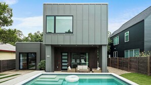 Een modern huis met twee verdiepingen, een zwembad, terras en omheinde tuin.