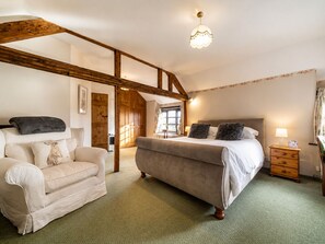 Een slaapkamer met een bed, een stoel, een nachtkastje en een houten balkenplafond.