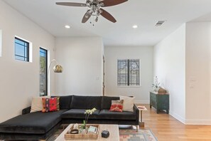 Un salon moderne avec un canapé d’angle, un ventilateur de plafond et une petite table d’appoint.