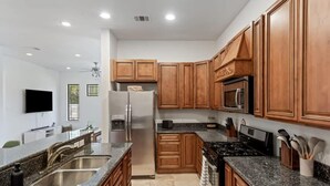 Una cocina moderna con encimeras de granito, armarios de madera, refrigerador, microondas y estufa a gas.