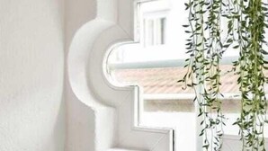 A window with a white geometric frame, a hanging plant, and three cacti on a white shelf. - Captivate Studio w/ Balcony | Clérigos by HostWise (Porto)