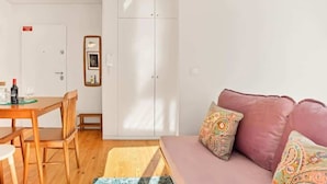 A room with a wooden dining table, chairs, a sofa with patterned cushions, a wardrobe, and a door with a sign. - Captivate Studio w/ Balcony | Clérigos by HostWise (Porto)