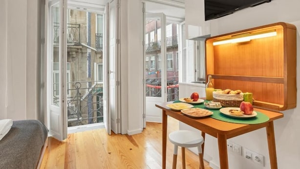A small, bright room with a wooden table set for breakfast, a bed, and a TV mounted on the wall. - Captivate Studio w/ Balcony | Clérigos by HostWise (Porto)