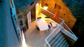 Una escalera conduce a un balcón con una mesa y sillas, techo de paja y pared de piedra.