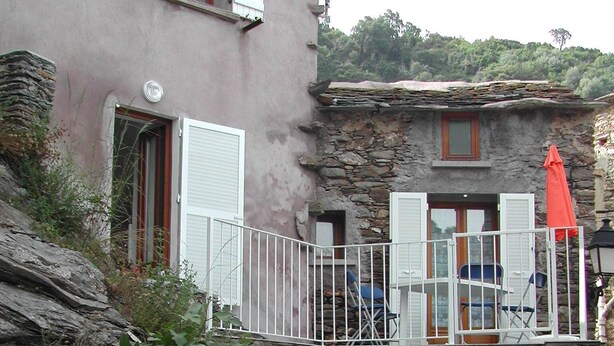 Una escalera de piedra que lleva a un edificio con balcón, rodeado de vegetación.