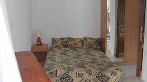 Un dormitorio pequeño y ordenado con cama, mesita de noche, lámpara y un banco de madera.